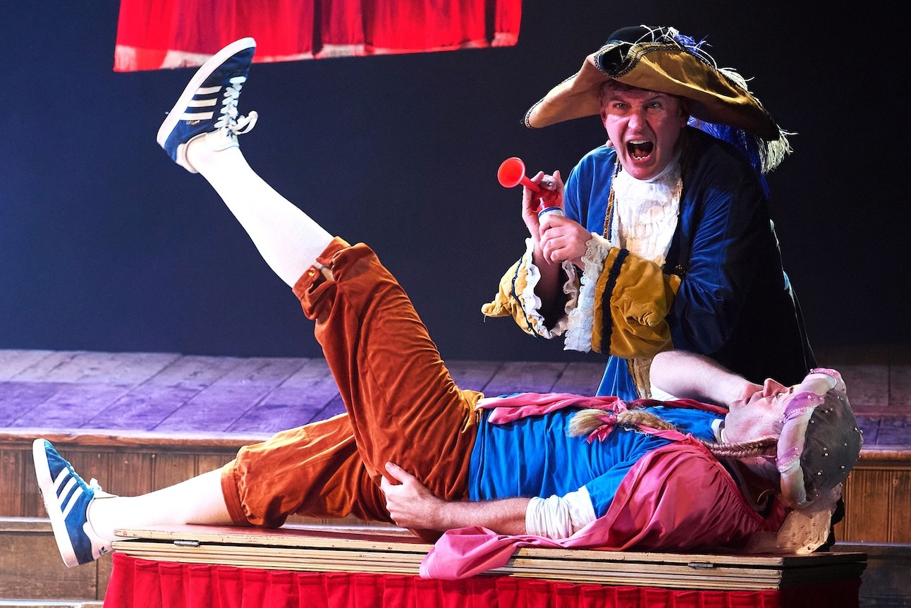 Two actors in colourful costumes perform energetically on stage at Wilton's Music Hall.