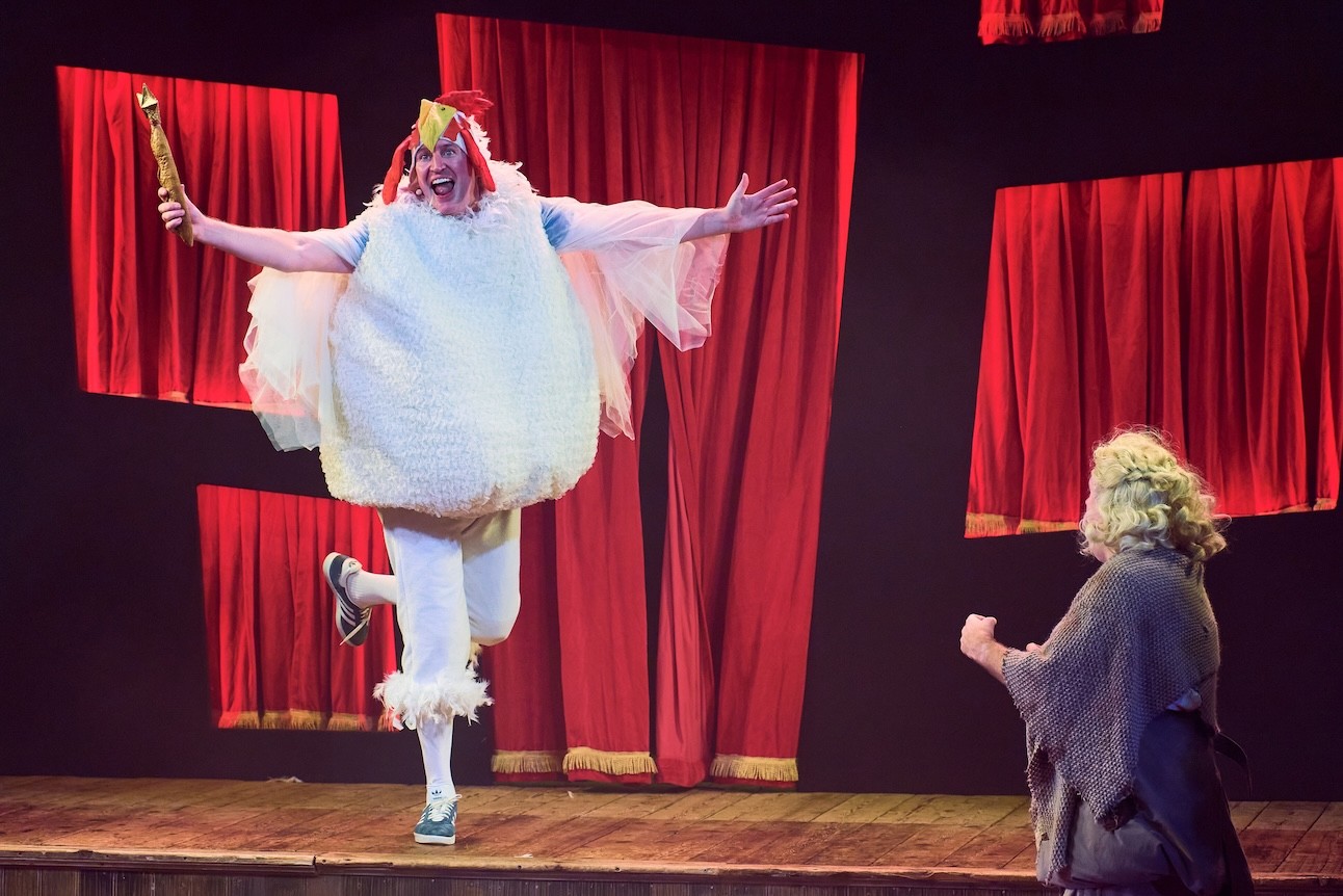 Two actors in colourful costumes, one dressed as a bird perform energetically on stage at Wilton's Music Hall.