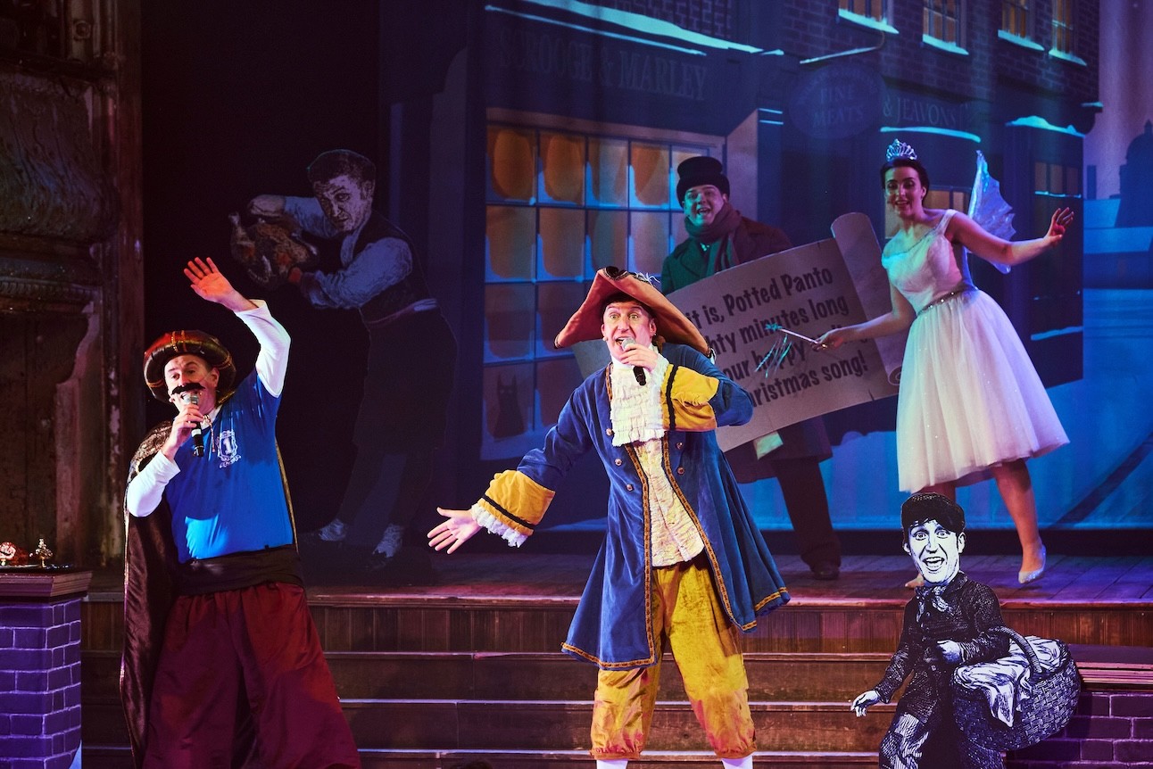 Two actors in colourful costumes perform energetically on stage at Wilton's Music Hall.