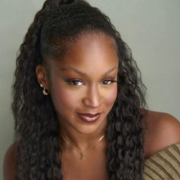Smiling woman with long, wavy hair and hoop earrings against a neutral background.