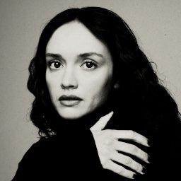 A person with long dark hair poses against a neutral background, looking directly at the camera.