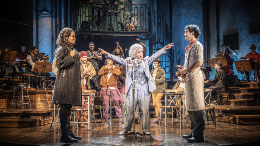 Hermes points at Orpheus and Eurydice in front of a packed stage