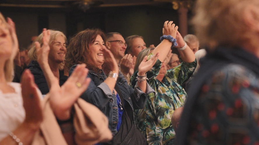 An audience member stood up clapping and smiling with other audience members around her also applauding